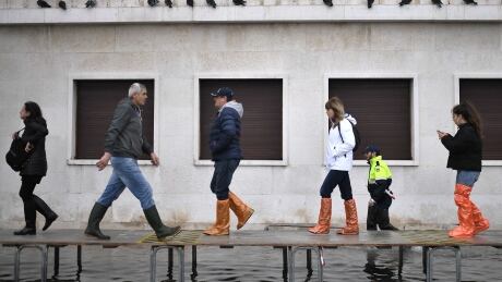 People walk on a footbridge across a flooded street after an exceptional overnight "Alta Acqua" high tide water level, on November 13, 2019 in Venice. - Venice was hit by the highest tide in more than 50 years late November 12, with tourists wading through flooded streets to seek shelter as a fierce wind whipped up waves in St. Mark's Square. (Photo by Marco Bertorello / AFP) (Photo by MARCO BERTORELLO/AFP via Getty Images) 1182108922