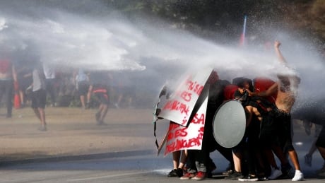 Anti-government protesters challenge a police water cannon spray in Santiago, Chile, Friday, Nov. 15, 2019. Students in Chile began protesting nearly a month ago over a subway fare hike. The demonstrations have morphed into a massive protest movement demanding improvements in basic services and benefits, including pensions, health, and education. Chile Protests