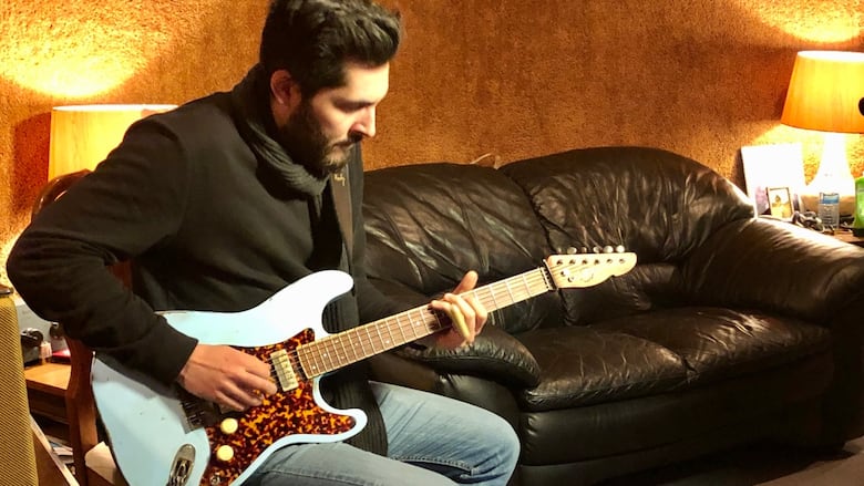 A man with dark hair plays a guitar.