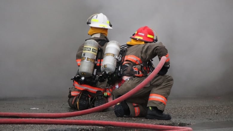 Two firefighters point a hose at smoke and flames.
