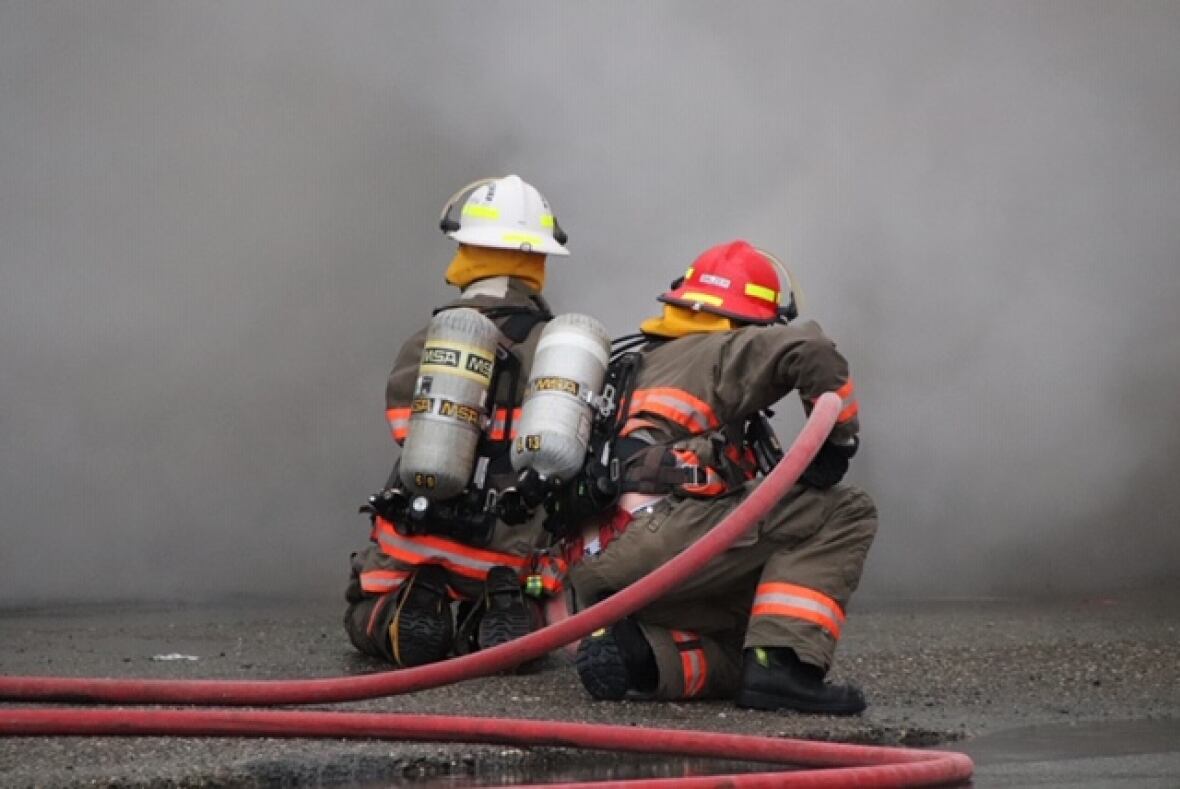 Two firefighters point a hose at smoke and flames.