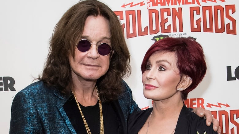 A man stands next to a woman while posing for a photo against a backdrop that reads "Metal Hammer Golden Gods."