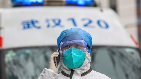 In this Sunday, Jan. 26, 2020 photo, a nurse in protective gear talks on her phone near an ambulance in Wuhan in central China's Hubei Province. A new viral illness being watched with a wary eye around the globe accelerated its spread in China on Sunday with 56 deaths so far, while the U.S. Consulate in the city at the epicenter announced it will evacuate its personnel and some private citizens aboard a charter flight. China Outbreak