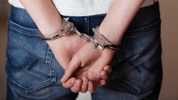 A person in a white shirt and jeans is handcuffed. 