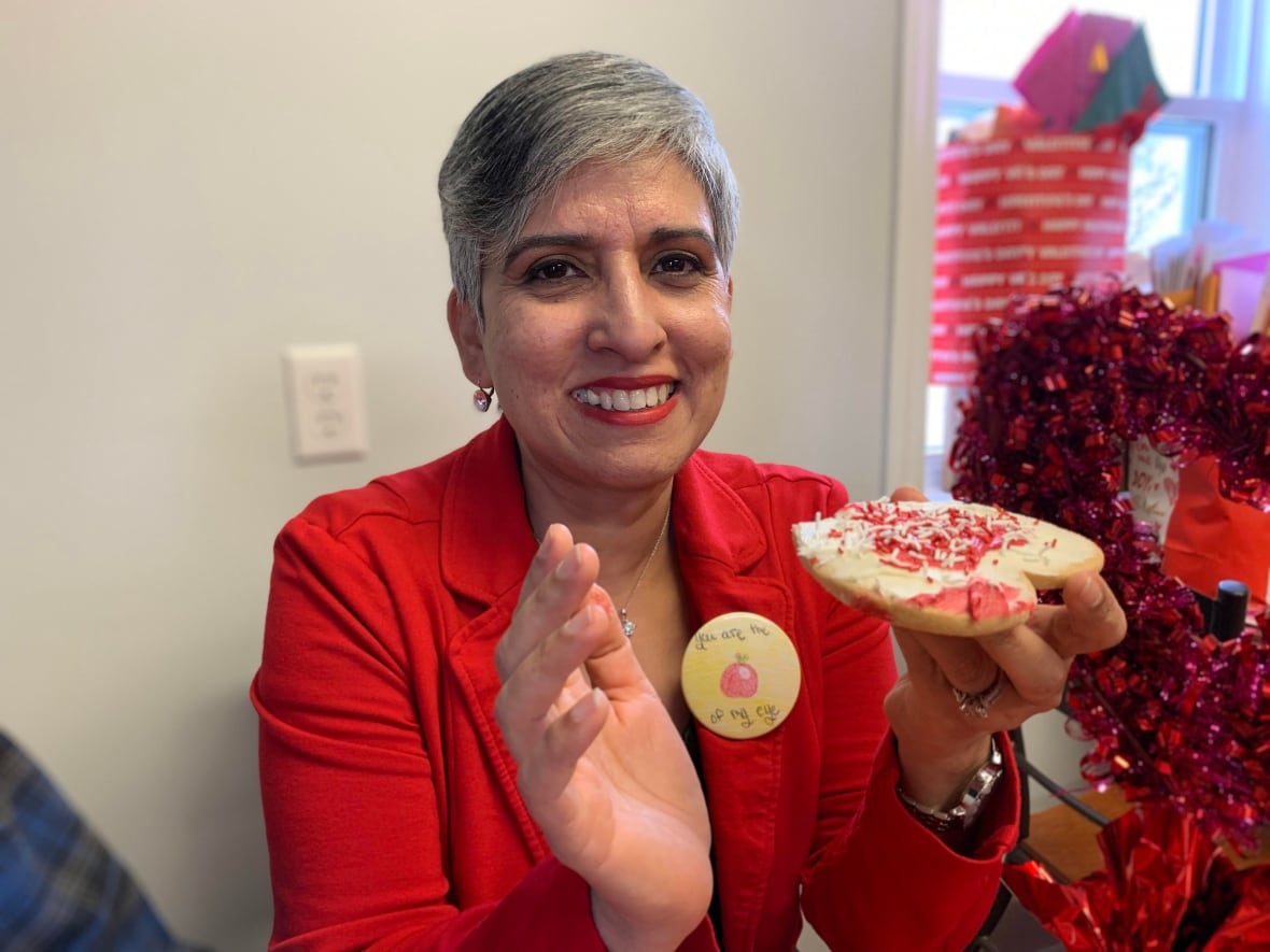 A woman smiles while holding a heart-shaped cookie.