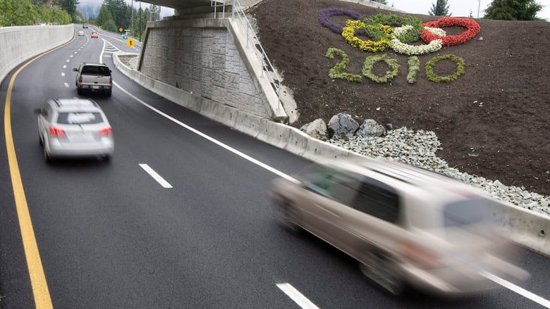 Cars drive past an Olympic ring pattern made out of flowers.