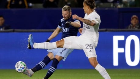 Vancouver Whitecaps midfielder David Milinkovic, left, shoots against LA Galaxy defender Rolf Feltscher during the first half of Vancouver's 1-0 win on Saturday night. MLS Whitecaps Galaxy Soccer