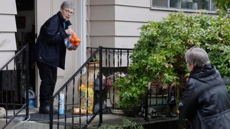 Pat McCauley gathers groceries and other items left on her porch by her daughter, Cheri Chandler, right, at her home, Friday, March 6, 2020, in Kirkland, Wash. Pat and her husband Bob have been self-quarantined in their home during the past week due to having visited friends at the Life Care Center nursing home — which has become the epicenter of the outbreak of the COVID-19 coronavirus in Washington state — several times in February. Nursing home COVID-19