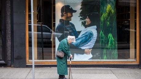 A woman waits for a bus on a near empty Robson Street in Vancouver on March 30, 2020. COVID-19 ROBSON STREET VANCOUVER