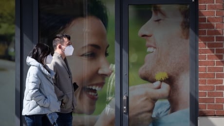 People wearing protective face masks walk past a photograph outside a drug store in Vancouver on Sunday, April 5, 2020. COVID Cda 20200405