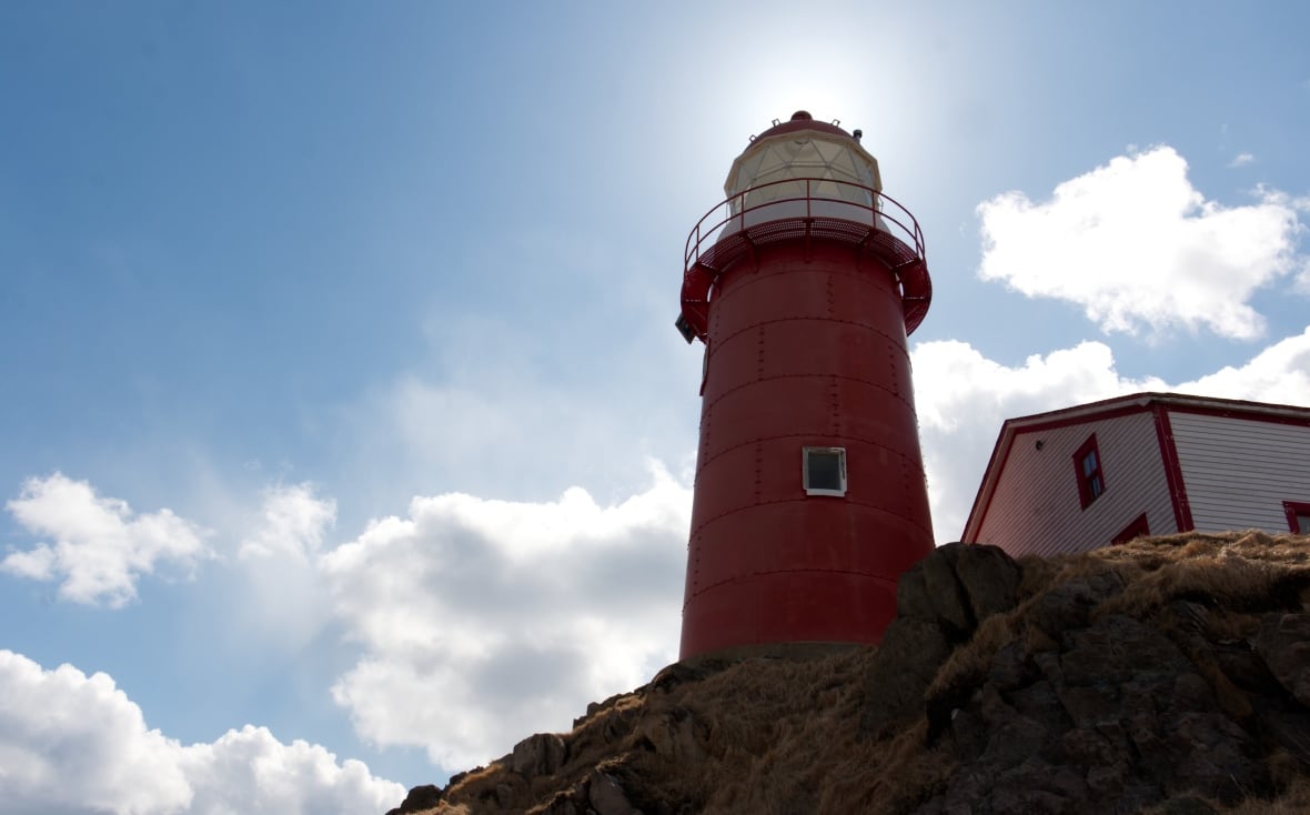 A photo of a large lighthouse on a hill. It's taken from a lower hill, as the lighthouse blocks the sun.