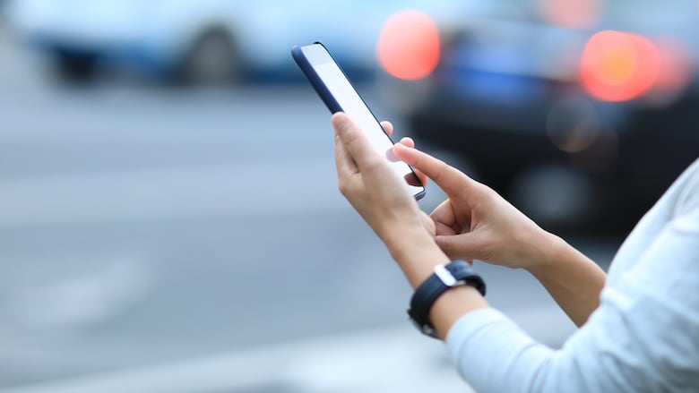A close-up of a person's hands holding a smartphone out in front of them, with vehicles in the background.