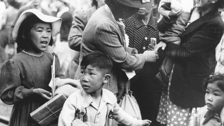 A black and white photo of children and women dressed well and looking scared.