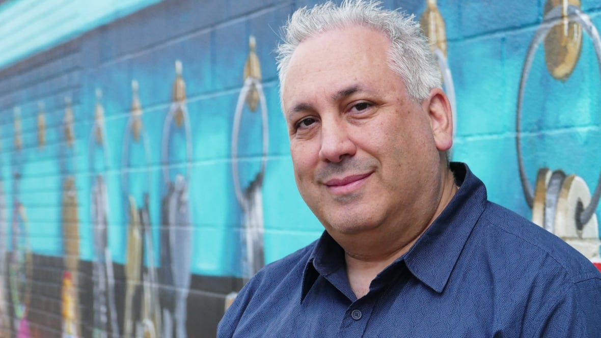 A man with short white hair is seen close up, from the shoulders up.