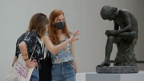 Visitors wearing face mask to prevent the spread of COVID-19, look at 'The Boy with Thorn" a first century B.C. bronze statue in the Rome's Capitoline Museums, Tuesday, May 19, 2020. In Italy, museums were allowed to reopen this week for the first time since early March, but few were able to receive visitors immediately as management continued working to implement social distancing and hygiene measures, as well as reservation systems to stagger visits to museums in the onetime epicenter of the European pandemic. (AP Photo/Alessandra Tarantino) Virus Outbreak Italy Reopening