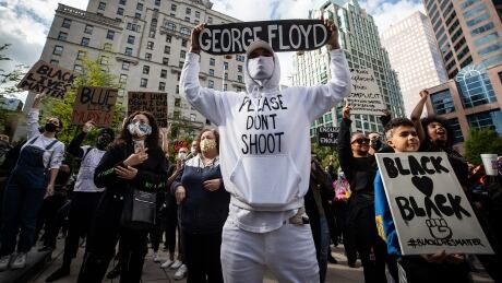 A man holds a skateboard bearing George Floyd's name above his head as thousands of people gather for a peaceful demonstration in support of Floyd and Regis Korchinski-Paquet and protest against racism, injustice and police brutality in Vancouver. Anti Racism Protest 20200531