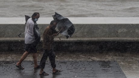 TOPSHOT - Two men carrying umbrellas walk on the Marine Drive under heavy rain in Mumbai on June 3, 2020, as cyclone Nisarga barrels towards India's western coast. - Mumbai authorities shut offices, banned small gatherings and told people to stay home on June 3 as the Indian megacity's first cyclone in more than 70 years approached. Cyclone Nisarga was expected to make landfall near the coastal town of Alibag, around 100 kilometres (60 miles) south of Mumbai, on June 3 afternoon, forecasters said. 1217233895