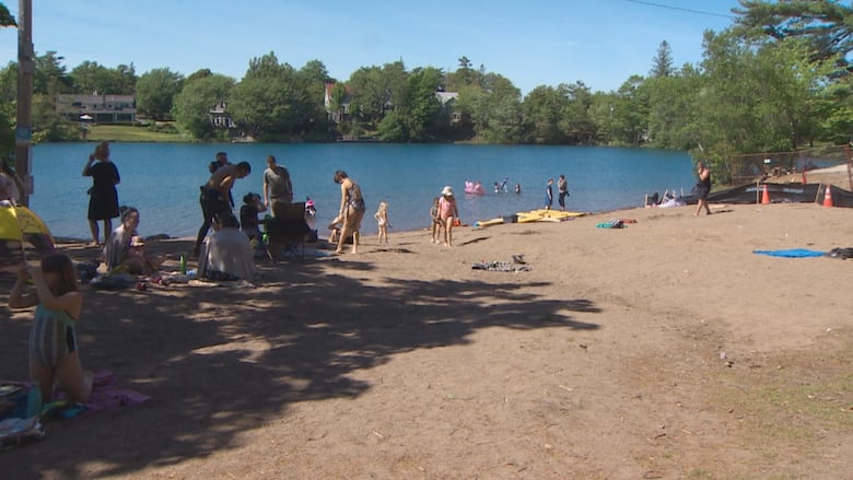 People gathered on a beach wearing swim suits and floaties. Chocolate Lake is in the background.