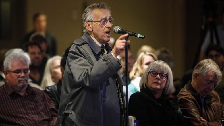 a man at a public meeting microphone talks and points