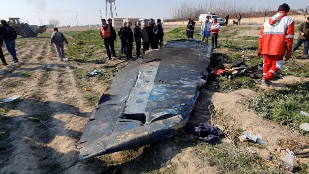 Broken plane part on ground, people surrounding it