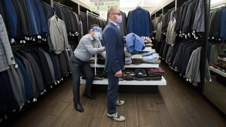 Head tailor Soheil Khorrami, left, demonstrates a safe way to fit a blazer for Joe Gagliardi at Tom's Place in Kensington Market during the COVID-19 pandemic in Toronto on Tuesday, June 2, 2020. THE CANADIAN PRESS/Nathan Denette COVID Retail Cda 20200602