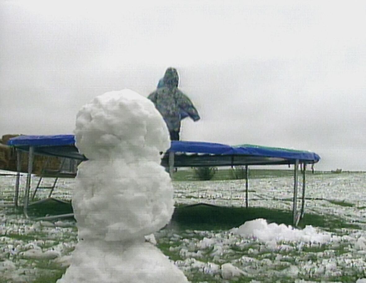 Snow figure in foreground of kids on trampoline