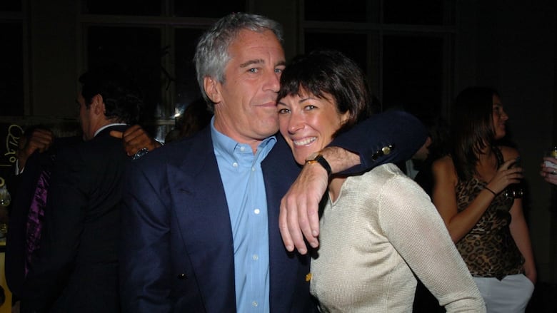 A white man with white hair stands with his arm around a woman with short black hair at night.