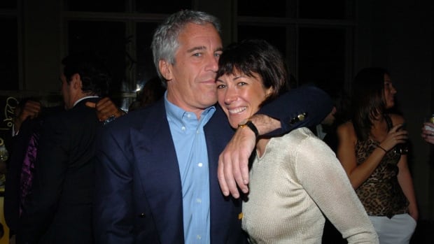A white man with white hair stands with his arm around a woman with short black hair at night.