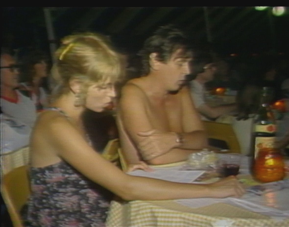 Man without shirt and woman in strapless top sit at a table