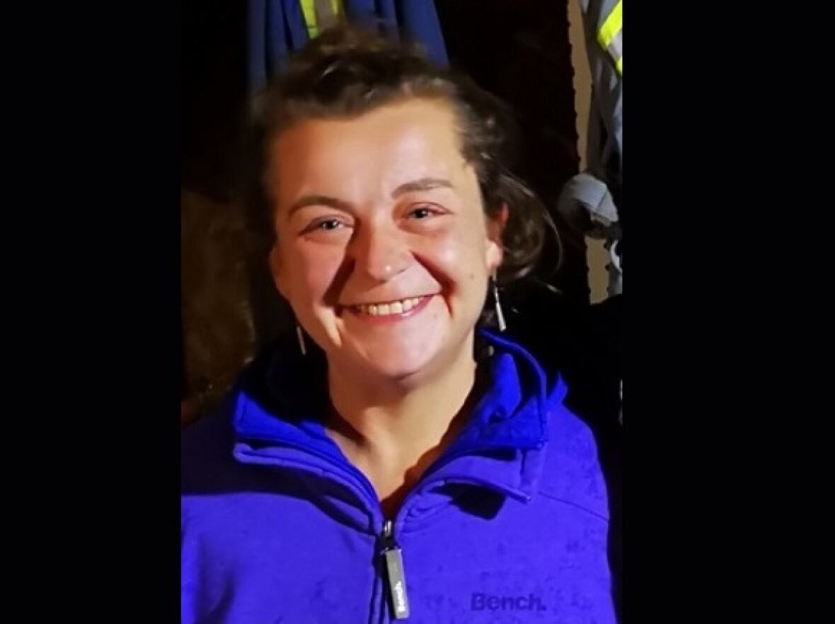 A smiling woman wearing a blue jacket with earrings.