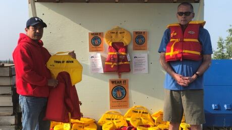 Senior Lifeguard Arn Guama, left, and Bob Everett, aquatics director for the Town of Inuvik, pose with life jackets at the town's new personal flotation device loaner station. Arn Guama & Bob Everett at Town of Inuvik's PFD Loaner Station