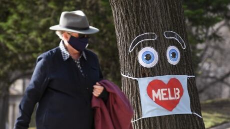 A man walks past a large face mask pinned to a tree in Melbourne on August 3, 2020 after the state announced new restrictions as the city battles fresh outbreaks of the COVID-19 coronavirus. - Australia's Victoria state imposed fresh, sweeping restrictions on August 2, 2020, including a curfew in Melbourne for the next six weeks, a ban on weddings, and schools and universities going back online in the coming days. 1227887859