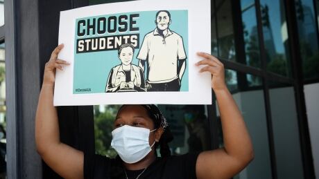 A demonstrator holds a sign Monday, Aug. 3, 2020, in Los Angeles. Parents, students, and teachers held a press conference and car caravan to call for a safe, fully funded, and racially just approach to reopening of Los Angeles schools. Virus Outbreak California Teachers