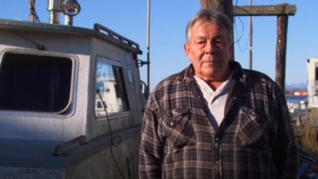 A man wearing a flannel poses for a photo in front of a boat.