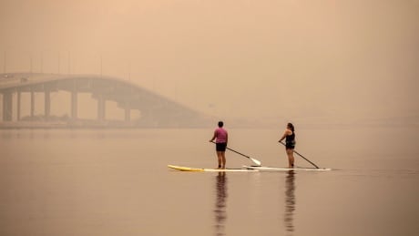 Summer activities for some continue as paddle boarders make their way towards the William R. Bennett Bridge on Okanagan Lake in Kelowna B.C. on Aug. 18, 2018. Thick smoke from the B.C. wildfires blanked the province, causing the air quality Health Index (AQHI) rated at 10+ in the Kelowna region, which is considered very high risk. kelowna smoke 2018