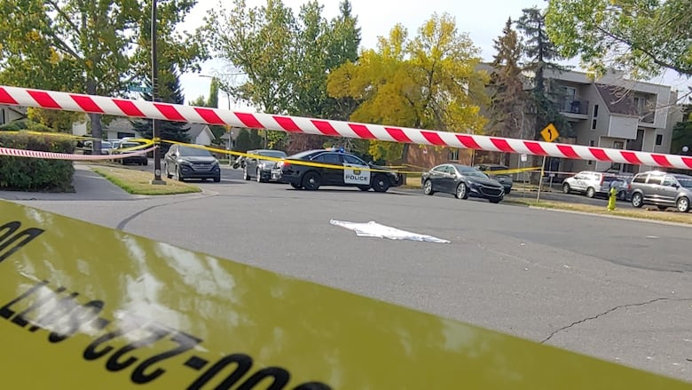 Police tape cordons off an area around a white sheet in the middle of a street. 