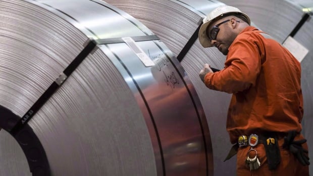 The Trump administration has withdrawn tariffs on Canadian steel and aluminum, but is threatening to reimpose aluminum tariffs after the Nov. 3 election. Seen here: a Dofasco employee looks at rolls of coiled steel in Hamilton in 2018. Man in orange jumpsuit and helmet inspects large coil of steel.
