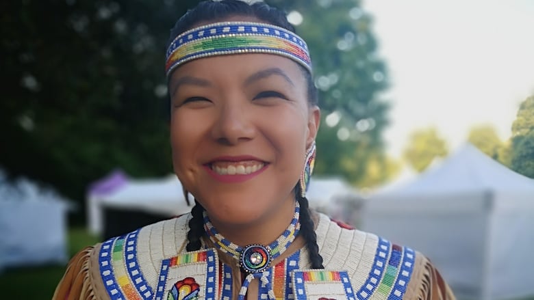 Deanne smiles at the camera in raindow beaded pow wow regalia.