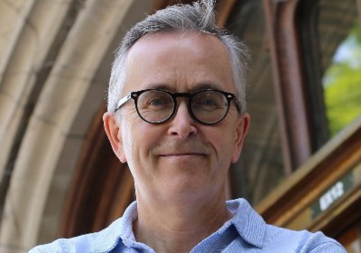 A grinning man with short grey hair and glasses