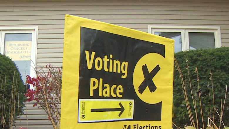 A yellow and black sign saying VOTING PLACE stands in front of a beige building.