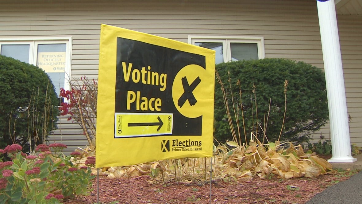 A yellow and black sign saying VOTING PLACE stands in front of a beige building.