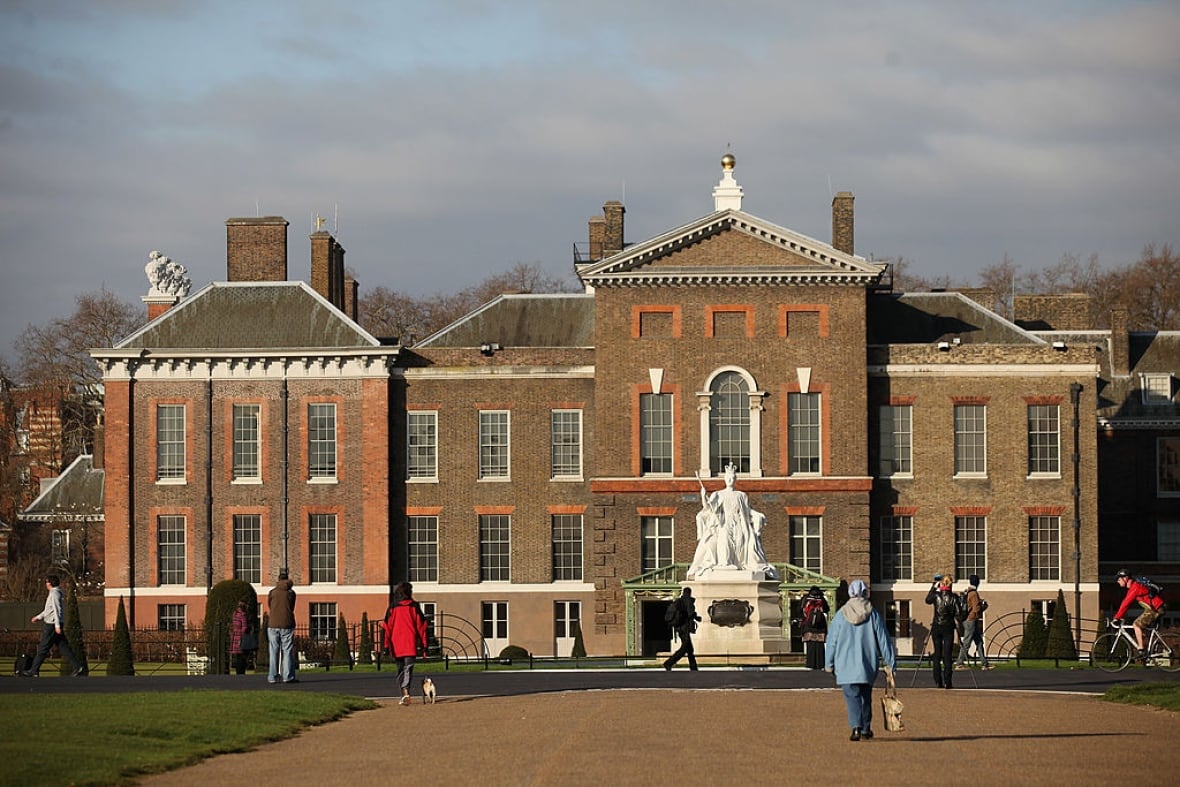 People walk in front of a large reddish-brown brick building.