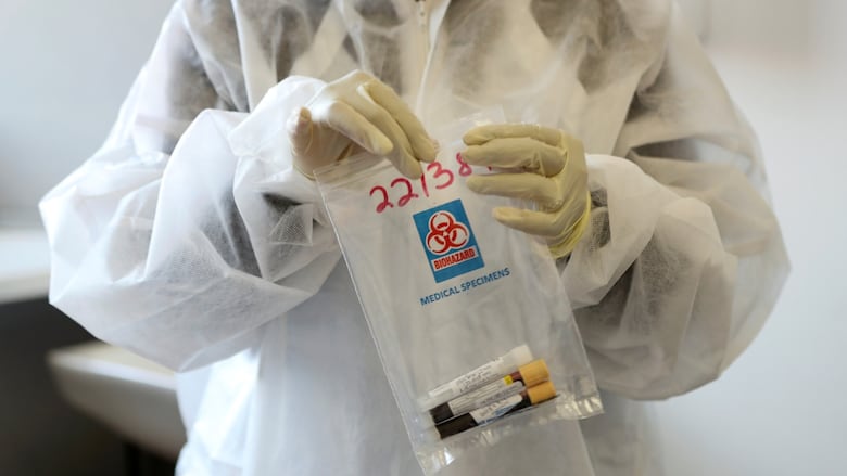 A person in a hazmat suit holding blood samples.