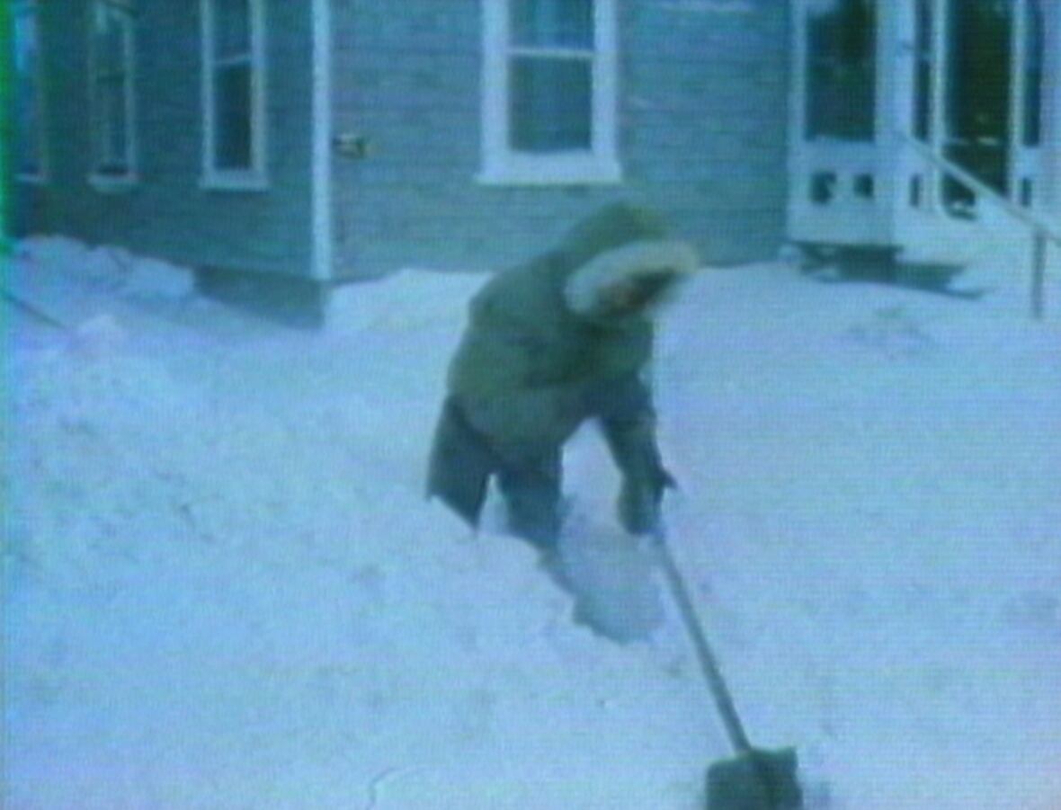 Man in jacket with fur-trimmed hood shovels a large amount of snow