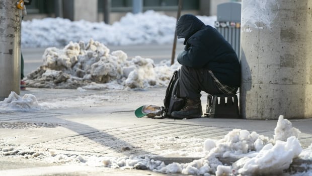 An individual panhandles on Bank Street in Ottawa. On Friday, four of the city's homeless shelters announced they would be unable to take new additions after multiple cases of COVID-19 were identified at their locations. A man sitting on the street.