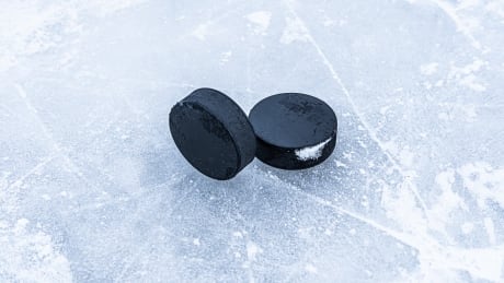 Two hockey pucks are laying on the ice. Hockey pucks