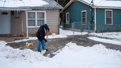 A Waco, Texas, resident clears snow from his driveway alongside his dog on February 17, 2021 as severe winter weather conditions over the last few days has forced road closures and power outages over the state. Millions of people were still without power on February 17 in Texas, the oil and gas capital of the United States, and facing water shortages as an unusual winter storm pummelled the southeastern part of country. The National Weather Service (NWS) issued a winter storm warning for a swath of the country ranging from east Texas to the East Coast state of Maryland. Man shovelling show in Waco, Texas on Feb. 17, 2021