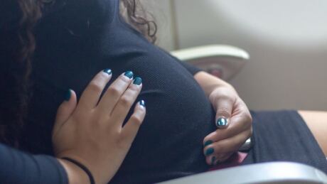 A pregnant woman sits in an airplane seat and holds her belly in this stock photo. Pregnant woman on airplane