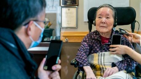 Ross Ha speaks to his 88-year-old mother through a glass door via his cellphone. This photo of them was taken on Tuesday, March 2, 2021. (Sam Nar/CBC) Ross Ha talks to his mother through a glass door