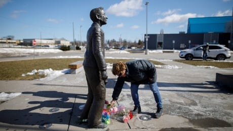 A woman places flowers at the foot of a statue depicting Walter Gretzky outside the Wayne Gretzky Sports Centre in Brantford, Ont. following the news of his passing. HKN Walter Gretzky 20210305